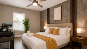 Ein Hotelzimmer mit Bett, Nachttischen, Deckenventilator, Fenster, Pflanze und Fernseher.