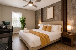Ein Hotelzimmer mit Bett, Nachttischen, Deckenventilator, Fenster, Pflanze und Fernseher.