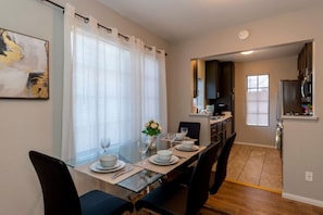 A dining area with a table set for four, a kitchen in the background, and a painting on the wall. - Modern Pet-Friendly 2BR | Near Strip & Chinatown (Las Vegas)