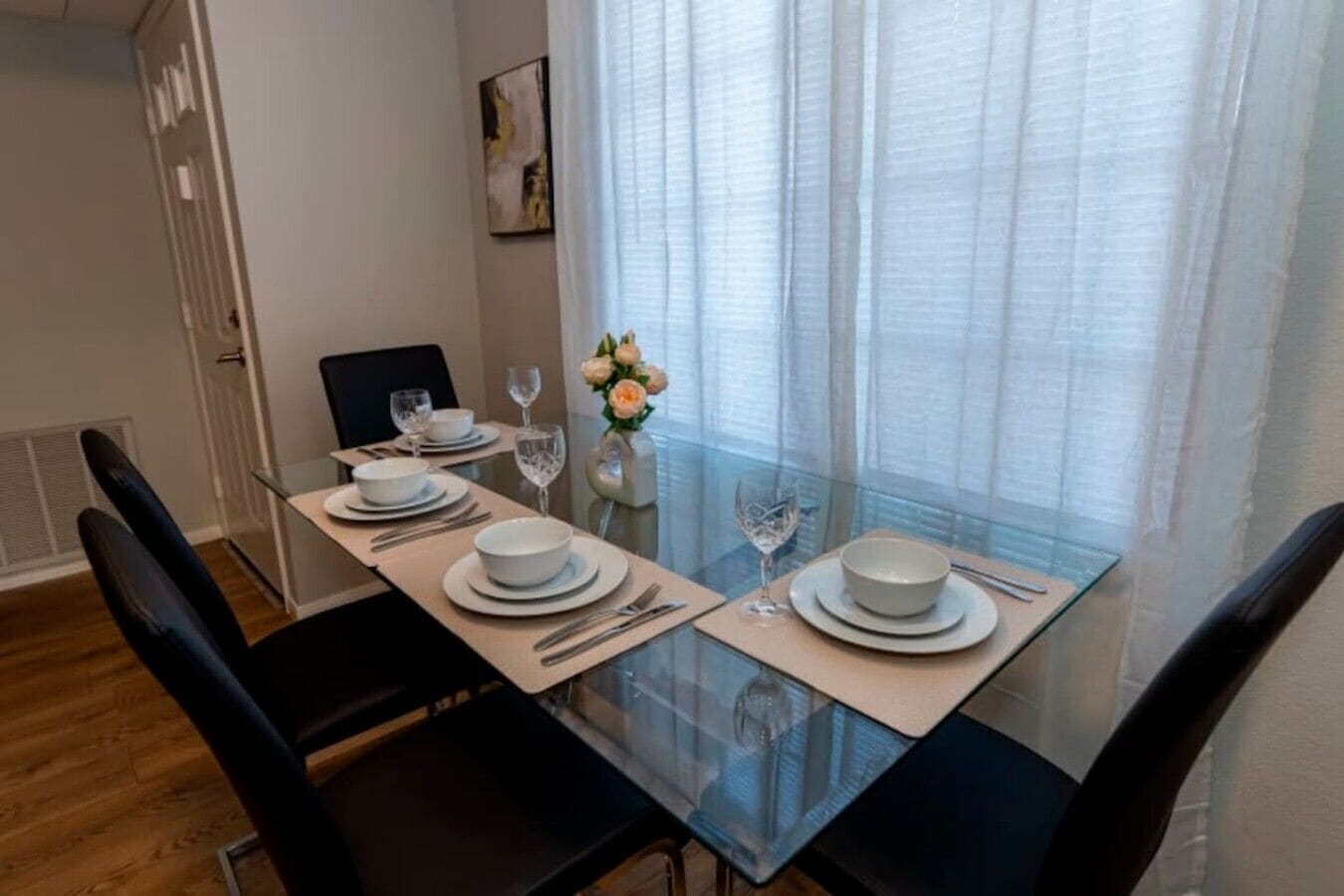 Un coin repas avec une table en verre, dressée pour quatre personnes, des chaises et un vase rempli de fleurs.