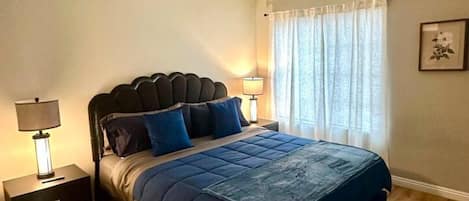 Ein Schlafzimmer mit einem Bett, Nachttischen, einem Fenster mit Vorhängen und einem Deckenventil.
