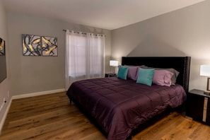 A bedroom with a large bed, a nightstand, a window with curtains, and abstract wall art. - Modern Pet-Friendly 2BR | Near Strip & Chinatown (Las Vegas)
