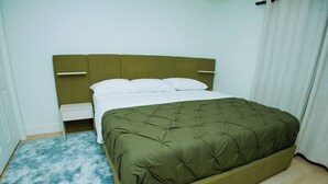 Ein Bett mit einem grünen, gesteppten Kopfteil, weißer Bettwäsche und einem flauschigen, blauen Teppich.