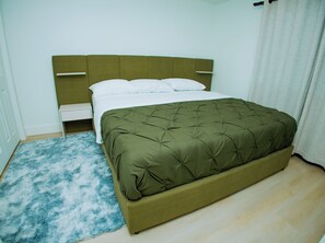 A bed with a green upholstered headboard, white bedding, and a blue shaggy rug. - Brand New 2BR Basement Suite +1 King Bed & Private Entrance (South Jordan)