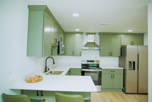 Eine kleine Küche mit grünen Schränken, einer weißen Arbeitsplatte, einem Edelstahlbackofen und einem Kühlschrank.
