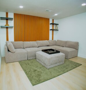 Ein Wohnzimmer mit Ecksofa, Couchtisch, grünem Teppich und einer Wand mit vertikalen Holzlatten.