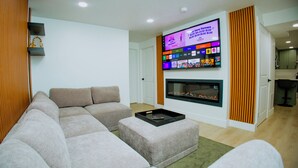 Ein Wohnzimmer mit einem Ecksofa, einem Flachbildfernseher über einem Kamin und einem kleinen Tisch mit Tablett.