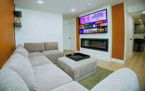 A living room with a sectional sofa, a flat-screen TV mounted above a fireplace, and a small table with a tray. - Brand New 2BR Basement Suite +1 King Bed & Private Entrance (South Jordan)