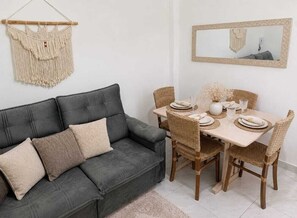 Un coin repas avec un canapé gris, une table à manger en bois, des chaises en osier et une décoration murale en macramé.