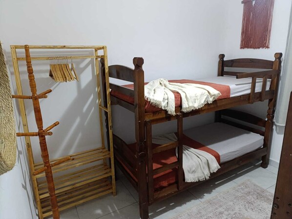 A bunk bed with a wooden ladder and a small shelf, a woven basket, and a wall-mounted macrame piece.