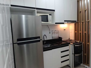 Une cuisine compacte équipée d’un réfrigérateur en acier inoxydable, d’un four à micro-ondes, d’une cuisinière à gaz et de meubles de rangement blancs.