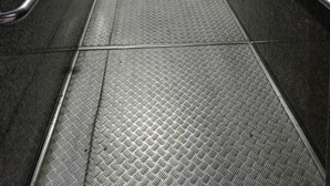 Un pasillo con barandillas metálicas, suelo texturizado e iluminación empotrada en el techo.