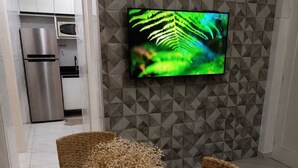 Un comedor con una mesa preparada para cuatro personas, una cocina moderna al fondo y un televisor de pantalla plana montado en la pared.