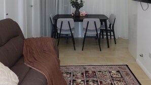 Ett vardagsrum med en brun soffa, ett matbord med stolar, en platt-TV som är monterad på väggen och en mönstrad matta på golvet.