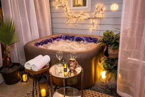 A hot tub with a purple interior, surrounded by plants, candles, and a table with glasses and a lantern. - East Austin, Walkable, Private Hot Tub and Parking (Austin)
