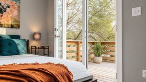 A bedroom with a bed, a nightstand, a lamp, a painting, and a view of the outdoors through a sliding glass door. - East Austin, Walkable, Private Hot Tub and Parking (Austin)