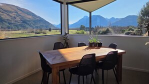 A dining area with a table and chairs, a view of mountains, and a large window. - Alpine Home Escape | Hot Tub & Mountain Views | Glenorchy (Glenorchy)