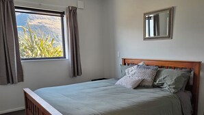 A bedroom with a bed, a window with curtains, a bedside table, and a mirror on the wall. - Alpine Home Escape | Hot Tub & Mountain Views | Glenorchy (Glenorchy)