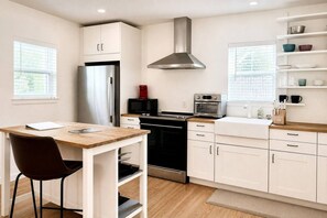 A modern kitchen with white cabinets, stainless steel appliances, and a wooden dining table. - King•Heart of East Downtown•Self Check-In (Austin)