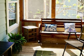 A wooden bench with a cushion, a small table, and a chair in a sunlit porch area. - King•Heart of East Downtown•Self Check-In (Austin)