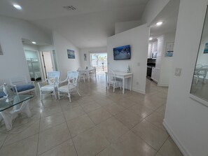 Amplia sala de estar con mesa y sillas de comedor, zona de cocina y vistas a través de una puerta abierta.