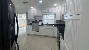 A modern kitchen with white cabinetry, a stainless steel refrigerator, and a black countertop.