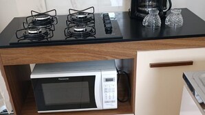 A kitchen with a gas stove, a microwave, a coffee maker, and a cabinet with drawers. - Cozy kitchenette (Araçuaí)