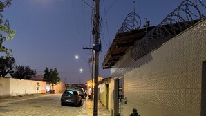 A paved street with a sidewalk, a parked car, and a building with a textured wall. - Cozy kitchenette (Araçuaí)