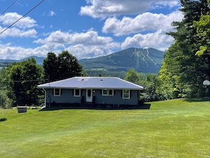 A house with a sloped roof, a front porch, and a lawn. - Quaint 2-bedroom apartment in East Burke (Burke)