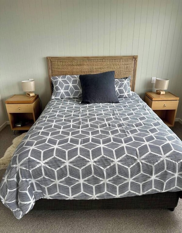 A bed with a geometric patterned bedspread, two bedside tables with lamps, and a wooden headboard.