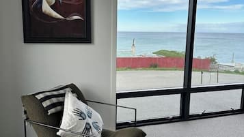 Ein Zimmer mit großem Fenster, einem gerahmten abstrakten Gemälde und einem Stuhl mit Metallgestell und Kissen.