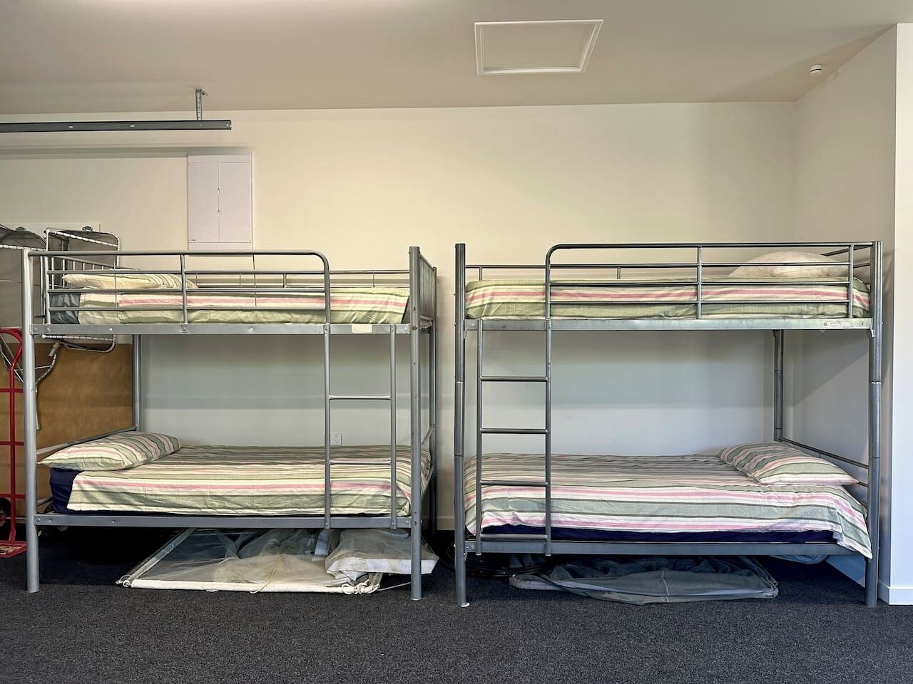 A room with two bunk beds, a red ladder, and a door in the background.