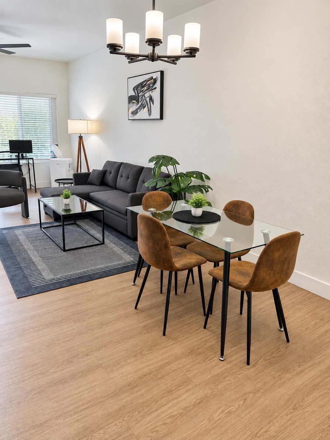Ett modernt vardagsrum med en soffa, ett matbord, stolar, ett soffbord, en lampa, en växt och en takfläkt.