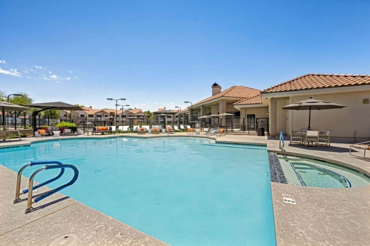 Una piscina con sillas de descanso y sombrillas, rodeada de edificios con techo de tejas.