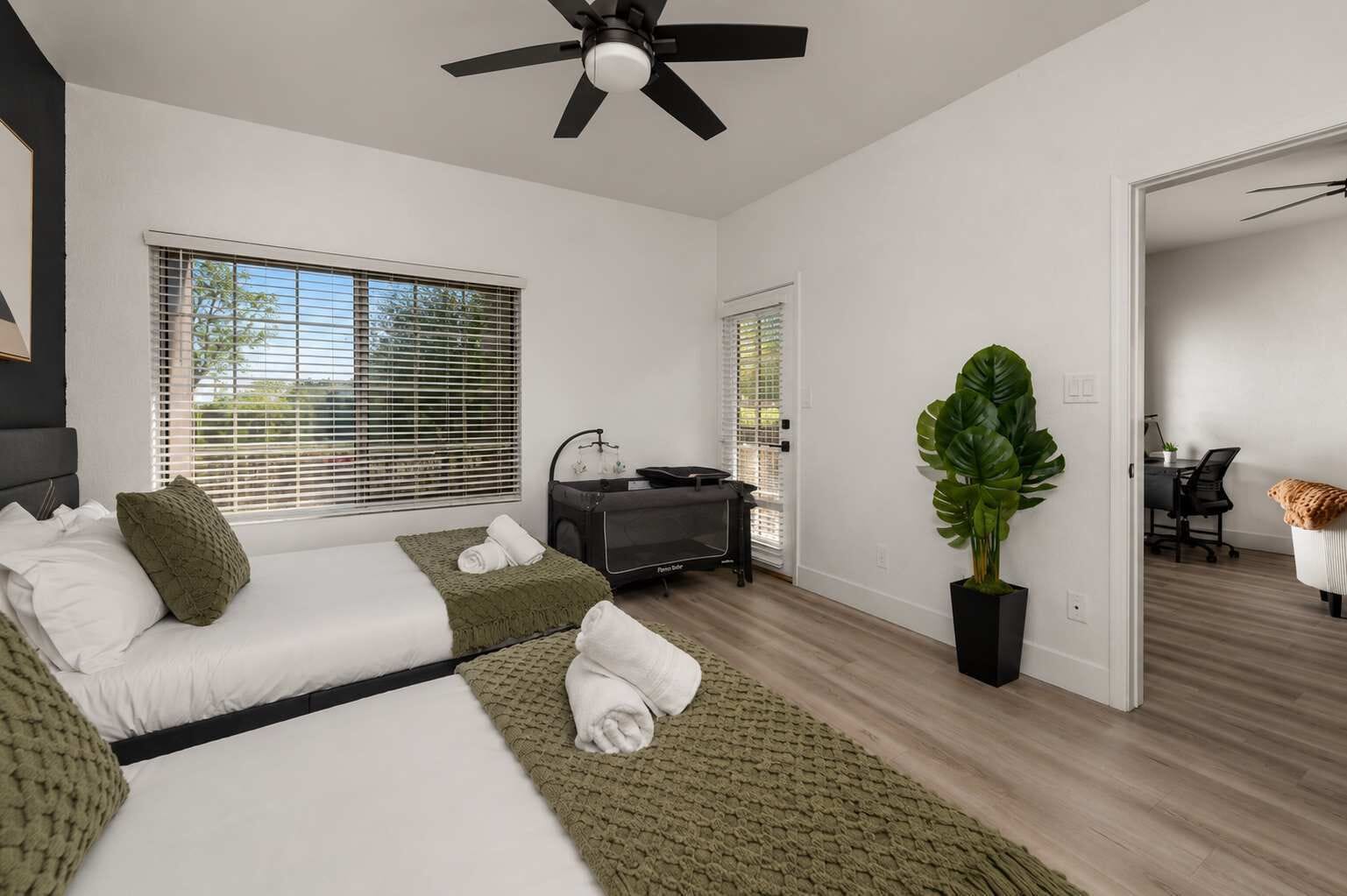 A modern bedroom with a bed, bedside tables, a desk, and a large plant.