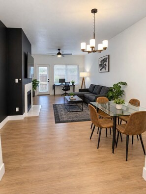 A modern living room with a sofa, dining table, and chairs, a fireplace, and a ceiling fan. - Stylish 2BR Retreat w Pool and Gym (Scottsdale)