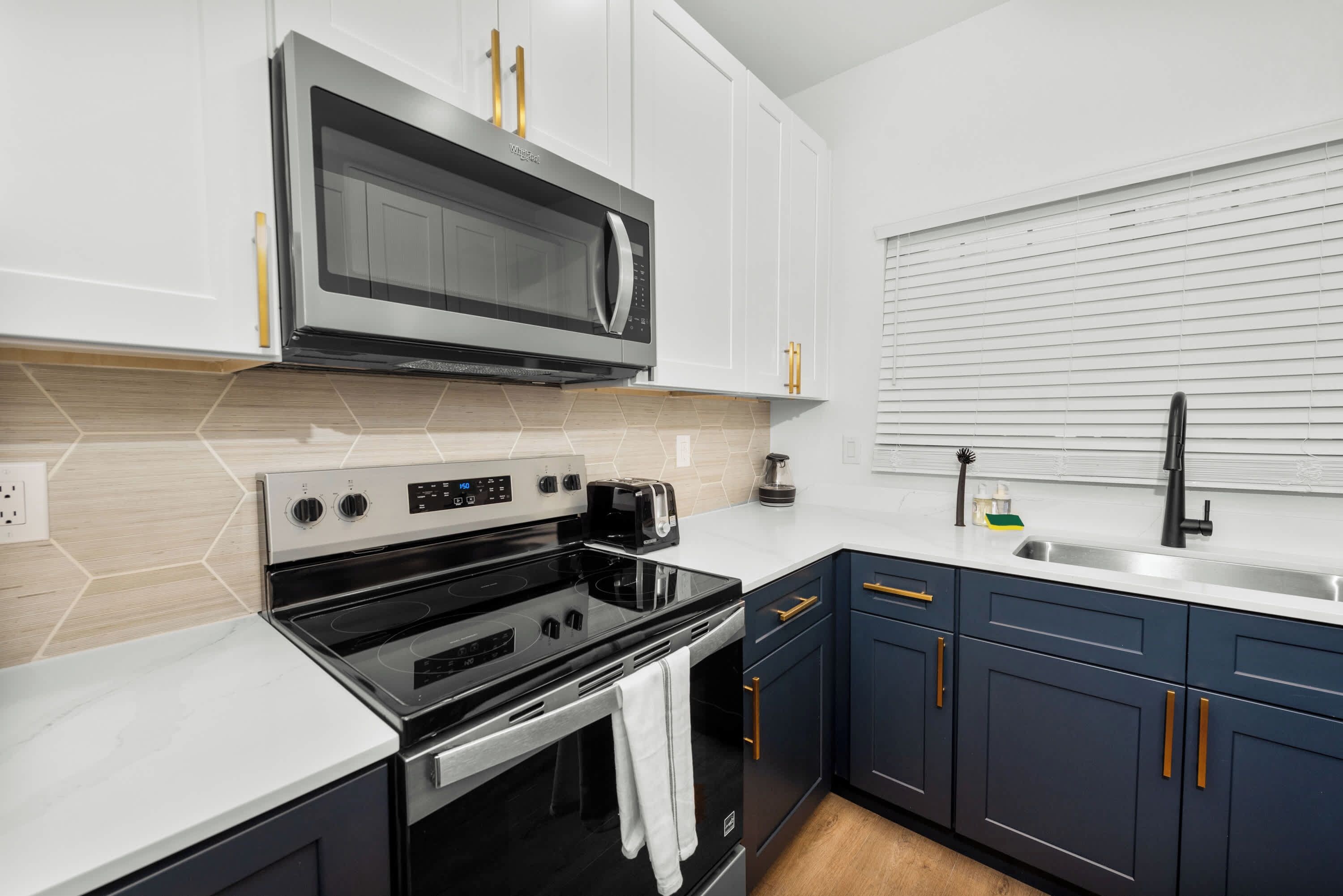 A modern kitchen with white cabinets, a stainless steel microwave, a black stove, and a sink with a faucet.