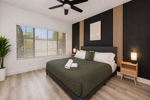 A modern bedroom with a bed, a ceiling fan, a bedside table with a lamp, and a window with blinds. - Scottsdale Retreat - 2BR Resort Condo with pool and Gym (Scottsdale)