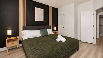 A modern bedroom with a large bed, bedside lamps, a headboard, and a door leading to another room.