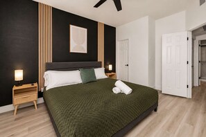 Een moderne slaapkamer met een groot bed, nachtlampjes, een hoofdeinde en een deur naar een andere kamer.