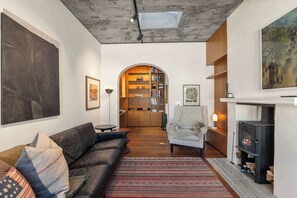 A modern living room with a leather sofa, a patterned rug, a fireplace, and a bookshelf. - The Sumner Escape - Sleeps 5, Walk to Beach (Christchurch)
