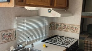 A compact kitchen with wooden cabinets, a gas stove, a sink, and a fire extinguisher.