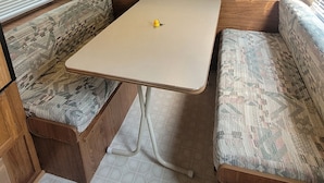 A compact RV interior with wooden cabinets, a central table, and patterned seating.