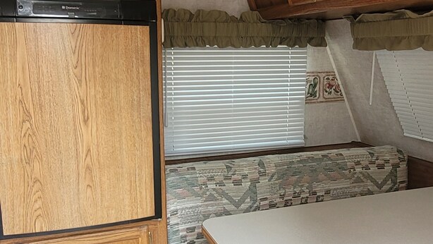 A compact RV interior with a kitchenette, a dining area, and a sleeping berth.