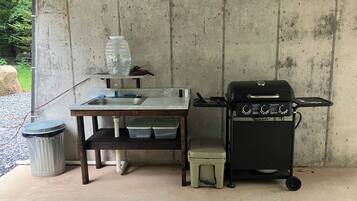 A concrete wall with a metal sink, a portable grill, and storage containers.