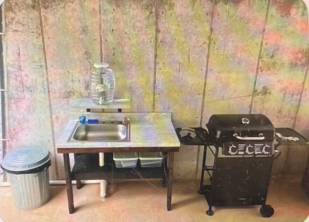 A small kitchen area with a sink, a trash can, and a portable grill.