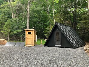 Uma cabana com uma latrina de madeira e uma estrutura de telhado preto numa área arborizada.