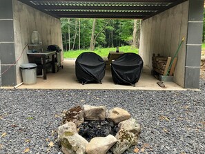 Un espacio al aire libre cubierto con dos parrillas, un contenedor de basura, dispensador de agua y un pozo de fuego rodeado de rocas.