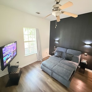 Ein Schlafzimmer mit Bett, Deckenventilator, Fernseher und einem Fenster mit Vorhängen.