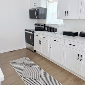 A modern kitchen with white cabinetry, a microwave, a stove, and a patterned rug. - Beautifully Renovated 3-Bedroom Home Minutes from Downtown Atlanta (Atlanta)